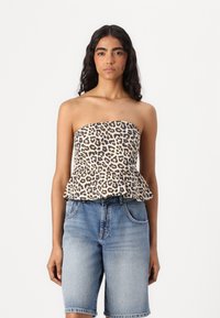 Top brez naramnic s peplum pasom v leopardjem vzorcu, izdelan iz lahkega materiala, v kombinaciji s svetlo modrimi jeans kratkimi hlačami s sproščenim krojem in žepi.