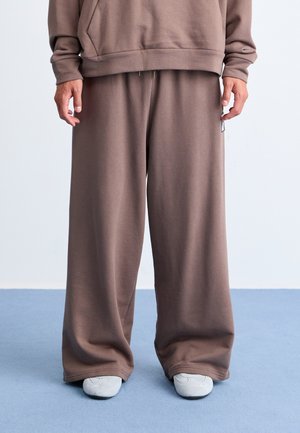 Brune oversized joggebukser laget av mykt stoff med en avslappet passform, med elastisk midje og mansjetter. Kombinert med lyse grå sko.