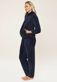 Navyblaues Fleece-Loungewear-Set mit hohem Kragen, herringbone Struktur, langen Ärmeln und Fronttaschen an der Jacke.