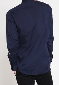 Granatowa koszula z długim rękawem z gładkiego materiału, z prostym tyłem, mankietami na guziki oraz subtelnymi detalami na rękawach.