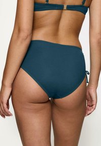 Wysokie, tealowe majtki bikini z bocznymi wiązaniami, gładki materiał i jednolity kolor. Charakteryzują się czystym, minimalistycznym designem, bez wzorów.