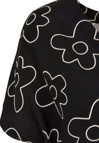 Tissu noir avec de grands motifs floraux abstraits en contour blanc, montrant un gros plan du manchon et de la zone de l'épaule d'un vêtement.