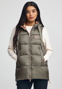 Oliwkowa pikowana kamizelka z kapturem, zapinana na zamek, z różową podszewką oraz naszywką z logo, wyposażona w regulowane sznurki i boczne kieszenie.