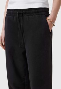 Zwarte sweatpants van zacht materiaal met een elastische tailleband, trekkoord, zijzakken en een subtiele logo-detail op de heup.