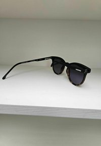 Zwarte en schildpadbril met ronde lenzen, een slank ontwerp en metalen accenten aan de armen, gelabeld "KOMONO."