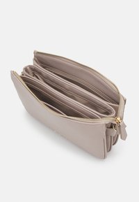 Pochette en cuir gris clair avec fermeture à glissière dorée, comprenant trois compartiments. Texture lisse et design minimaliste avec de subtils détails de couture.