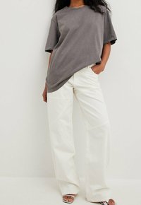 Harmaa ylisuuri t-paita lyhyillä hihoilla yhdistettynä leveälahkeisiin valkoisiin housuihin. Asusteessa on pehmeä kangas ja minimaalinen yksityiskohtaisuus.