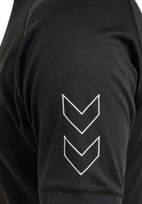 Sort atletisk skjorte med glat stof, korte ærmer og tre hvide chevron-detaljer på skulderen.