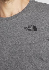 Šedé tričko vyrobené z bavlněné směsi, s kulatým výstřihem a malým černým logem "The North Face" na levé hrudi.