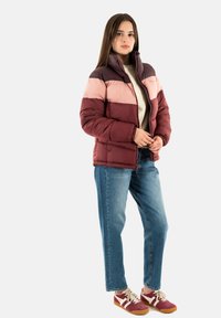Giubbotto imbottito con colletto alto, presenta blocchi di colore color maroon, rosa e viola scuro. Abbinato a jeans blu e sneaker rosse.