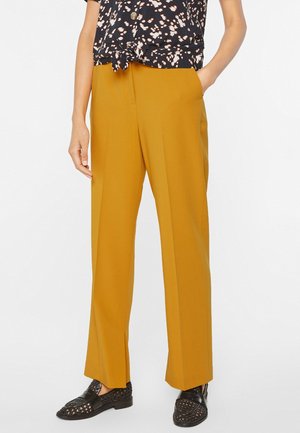 Pantalon jaune au design droit avec poches latérales. Le tissu semble lisse et léger, associé à un haut à motifs.