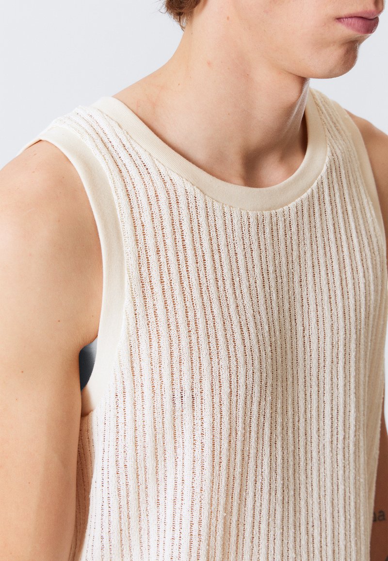 Ermeløs tanktopp laget av teksturert, lys beige stoff med vertikal ribbing. Rundet halsutringning og myk kant langs kantene.