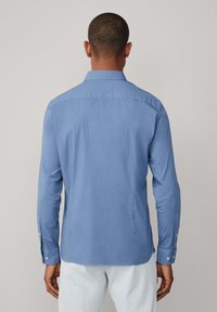 Camisa de manga larga azul claro con cuello abotonado, que presenta una textura suave y un diseño ajustado. Detalles de botones en los puños.