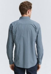 La camisa de hombre con botones presenta un patrón de cuadros en azul y blanco, mangas largas y un cuello doblado. La tela parece suave y ligera.