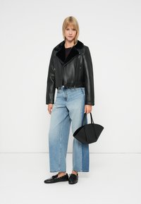 Juodas odinis trumpas švarkas su pūkine apykakle, derinamas su šviesiai mėlynomis plačiomis kelnėmis ir juoda kreiva rankine.