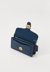 Borsa a tracolla in pelle blu navy con una chiusura dorata, vano con cerniera singola, tasca frontale e etichetta staccabile. Texture liscia e design strutturato.