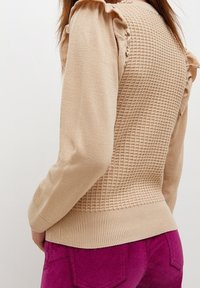 Pull beige avec un design de tricot texturé au dos, des accents de manches volants et un ourlet côtelé, assorti à un pantalon en suede rose.