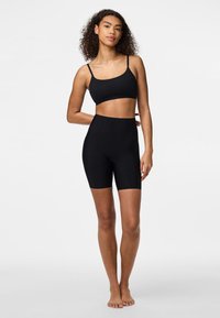 Set di reggiseno sportivo nero senza cuciture e pantaloni corti a vita alta. Il materiale è in tessuto elasticizzato. Presenta spalline sottili e orlo sopra il ginocchio.