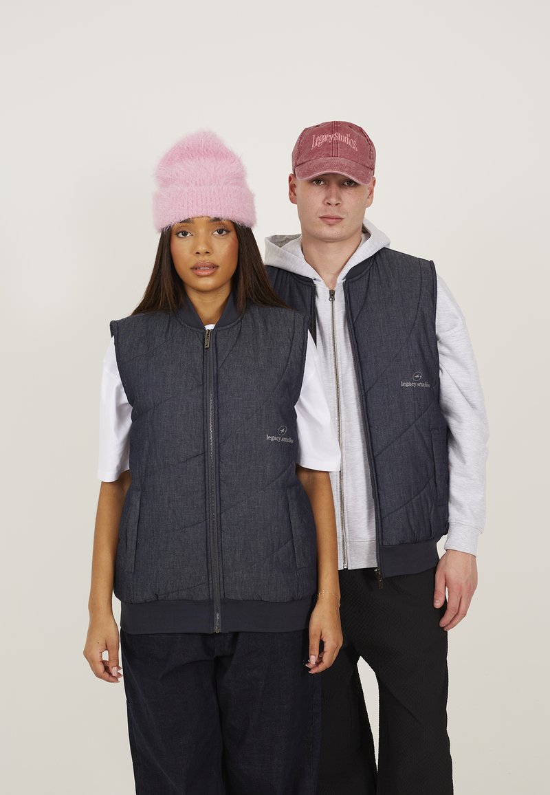 Due modelli indossano giubbotti in denim scuro abbinati con un motivo a trapunta, dotati di zip frontali. Un modello ha un berretto fluffy rosa; l'altro indossa un cappellino.