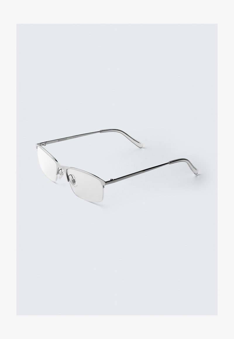 Metalliset silmälasit, joissa on tyylikäs suorakulmainen kehys. Hopeanvärinen viimeistely, jossa on kirkkaat linssit ja nenätyynyt. Ohut sanka, jonka päät ovat pyöristetyt.