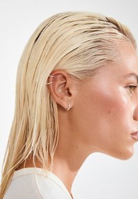 Stříbrné kroužkové náušnice a studenky na chrupavce u osoby s mokrými, rovnými, blond vlasy, zobrazené v profilu na světlém pozadí.