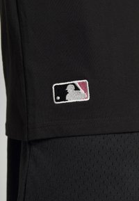 Svarta kläder med en vit, svart och röd broderad Major League Baseball-logga nära nederkanten.