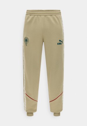 Pantaloni della tuta beige Puma King con vita elastica, righe laterali con logo, polsini a costine e loghi Puma e King verde scuro sul davanti.