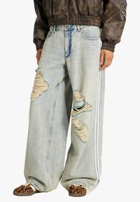 Jeans oversize azzurri chiaro con evidenti strappi e bordi sfrangiati. Presentano strisce laterali bianche e un classico design a cinque tasche.