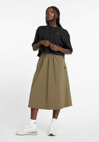 Camiseta negra recortada y falda midi verde oliva con cintura elástica y bolsillos laterales, combinada con zapatillas deportivas blancas.