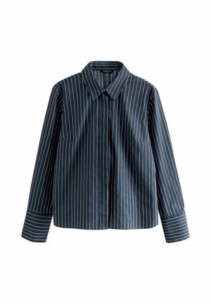 Tricou din stofă albastru închis, cu mâneci lungi, dungi verticale albe, guler ascuțit și manșete cu nasturi; are două buzunare frontale și o croială dreaptă.