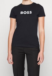 Camiseta de algodón negra con cuello redondo, que presenta la palabra "BOSS" en letras blancas gruesas en el pecho. Diseño ajustado.
