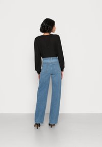 Jeans azuis de cintura alta e perna larga, feitos de denim, com bolsos frontais e traseiros, combinados com uma blusa de manga longa preta e saltos pretos.