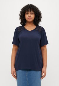 Navy blue short-sleeve top with a V-neck, featuring intricate lace accents on the shoulders and a relaxed fit. Smooth fabric with slight sheen.