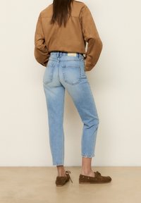 Jeans di denim blu chiaro con gamba affusolata, vita alta e due tasche posteriori. Abbinati a una giacca corta in suede marrone e scarpe marroni.