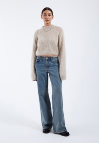 Beige fluffy cropped sweater with long sleeves, paired with high-waisted light blue jeans and black platform shoes. Plain background.