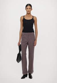 Svart tanktopp, rutete bukser i rød, blå og grå, med flat midje, og svarte hælboots. Modell som holder en svart veske.