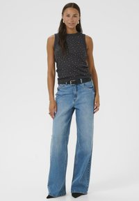 Black sleeveless top with white polka dots, paired with light blue wide-leg jeans. Black belt and sleek black shoes complete the outfit.