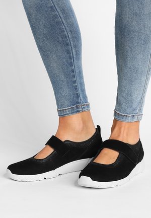 Sorte sportssko i ruskind med velcrolukning og rund tå, kombineret med blå skinny denimjeans. Hvid sål.