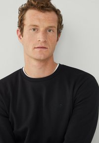 Sweatshirt noir en coton avec un col rond et des manches longues. Présente un petit logo discret sur la poitrine. Texture lisse.