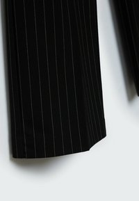 Zwarte, gestreepte broek met een gladde textuur. Kenmerkt zich door subtiele groene stiksels langs de naden en een recht model.