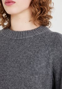 Szary, dziany sweter z okrągłym, prążkowanym dekoltem, miękką teksturą i minimalistycznym designem, odsłaniający ramię i górną część dekoltu.