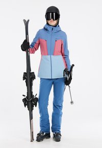 Abbigliamento da sci con giacca impermeabile blu e rosa, pantaloni blu, guanti neri, un casco e attrezzatura da sci. Design elegante e moderno.