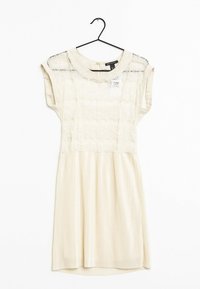 Robe crème avec un haut en dentelle et une jupe rayée. Caractérisée par des manches courtes, un col rond et un ourlet légèrement arrondi. Suspendue à un crochet noir.