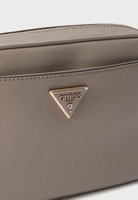 Borsa in pelle grigia con texture, con un accessorio triangolare in oro come logo sulla parte anteriore, dotata di chiusura a zip e design piatto.