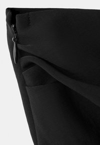 Gros plan d'un coin de sac à dos en tissu noir montrant une fermeture éclair et un détail de tissu plié.
