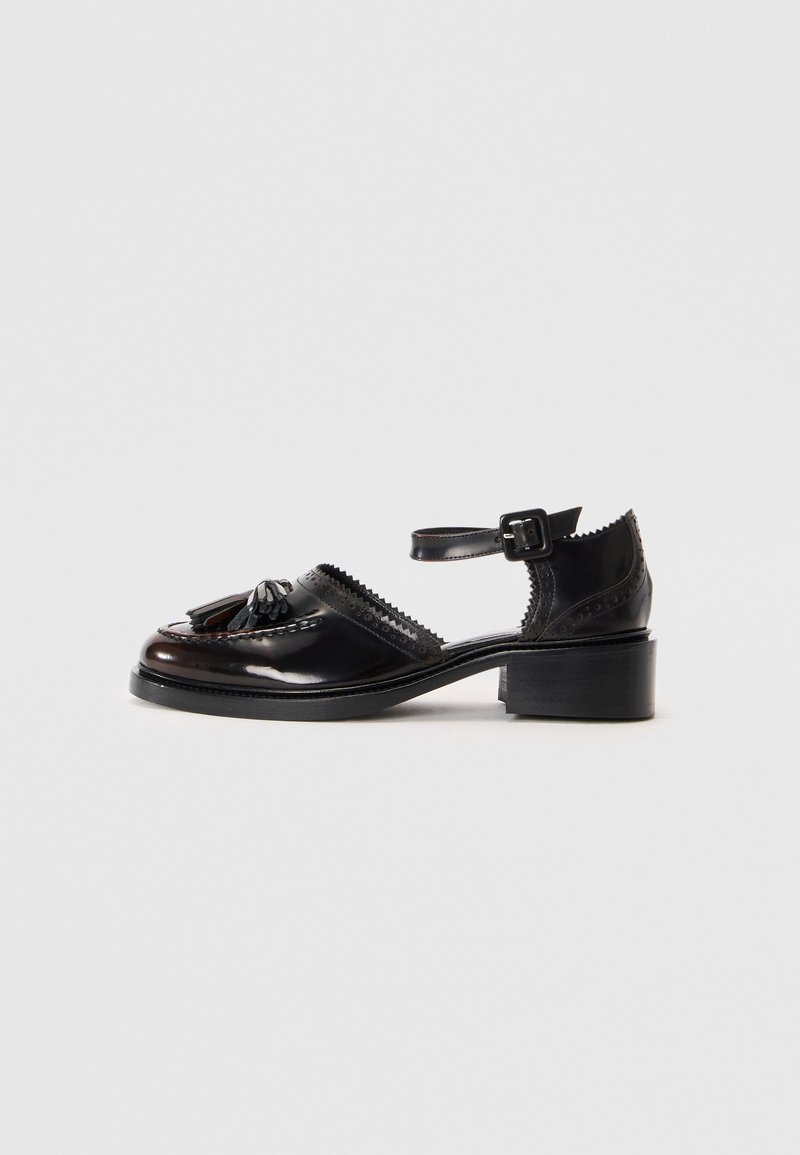Sapatos de couro pretos com um salto baixo em bloco, apresentando um tassel decorativo, bordas com recortes e uma tira ajustável no tornozelo.