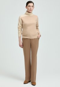 Beiger Rollkragenpullover mit glatter Textur, kombiniert mit hellbraunen geraden Hosen und braunen Schuhen. Einfaches Design, keine Muster.