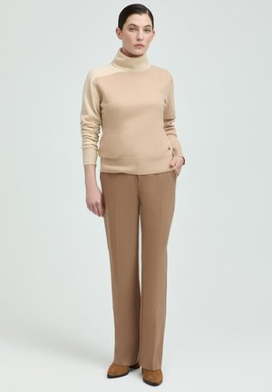 Beiger Rollkragenpullover mit glatter Textur, kombiniert mit hellbraunen geraden Hosen und braunen Schuhen. Einfaches Design, keine Muster.