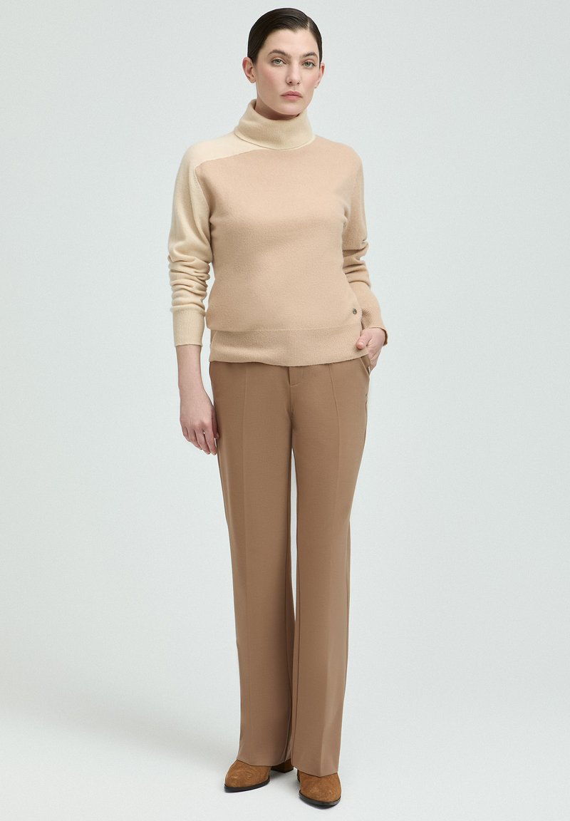 Beiger Rollkragenpullover mit glatter Textur, kombiniert mit hellbraunen geraden Hosen und braunen Schuhen. Einfaches Design, keine Muster.