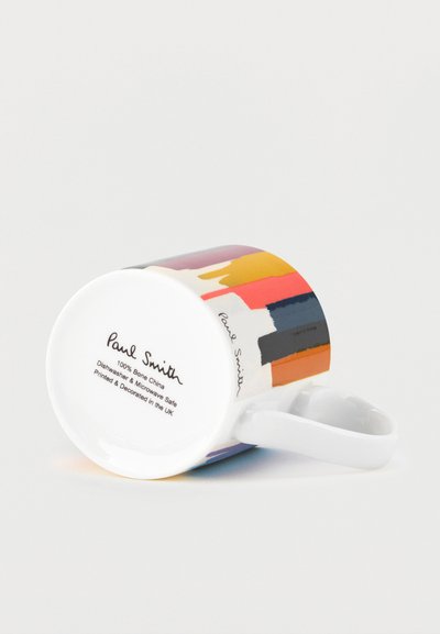 Tasse en céramique Paul Smith rayée multicolore couchée sur le côté, montrant le texte au bas avec le nom de la marque et les instructions d'entretien.